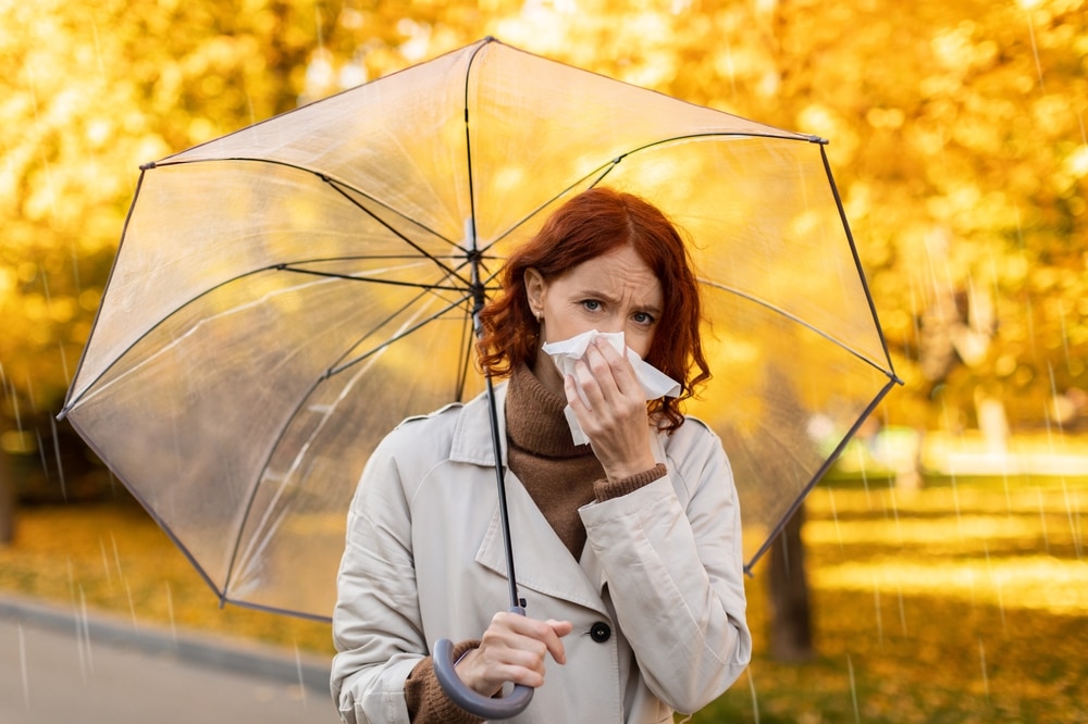 Woman standing under her umbrella in the rain blowing her nose